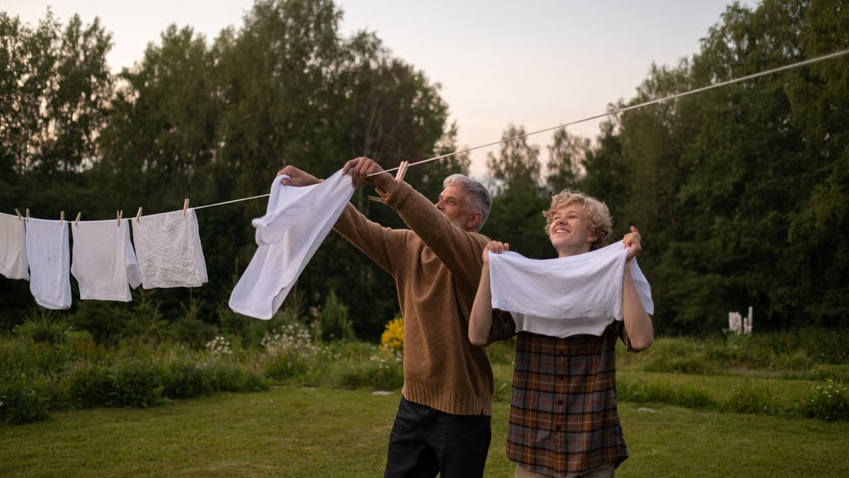 A joyful moment as grandfather and grandson hang laundry on a line in a lush summer garden.